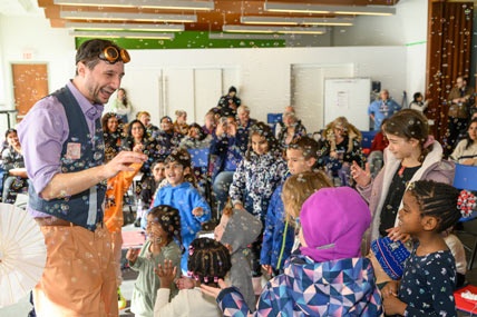 A male performer in dressed in pastel colours does a bubble performance for an audience of happy children at PAMA